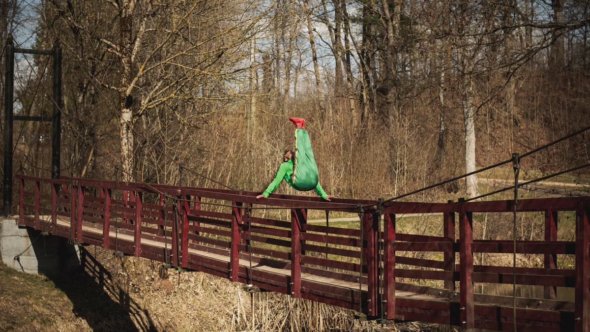 An athlete in green and red performs a dynamic gymnastic pose on a bridge outdoors in Vilnius.